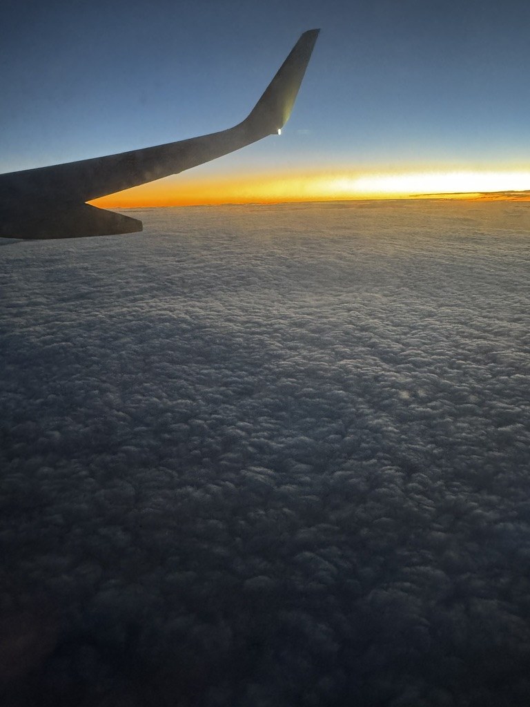 An airplane wing at sunset above the clouds