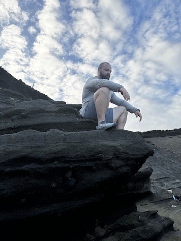 Ian sitting on the rocks by the sea